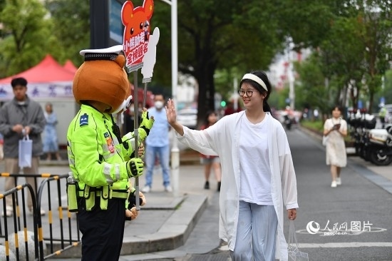 6月7日上午9時，隨著鈴聲的響起，2023年江西高考正式開考，江西省的53.57萬考生以縣（區(qū)）為單位隨機安排在全省256個考點、18968個考場參加高考。圖為“小熊交警”和考生擊掌鼓勵。 人民網(wǎng)記者 時雨攝