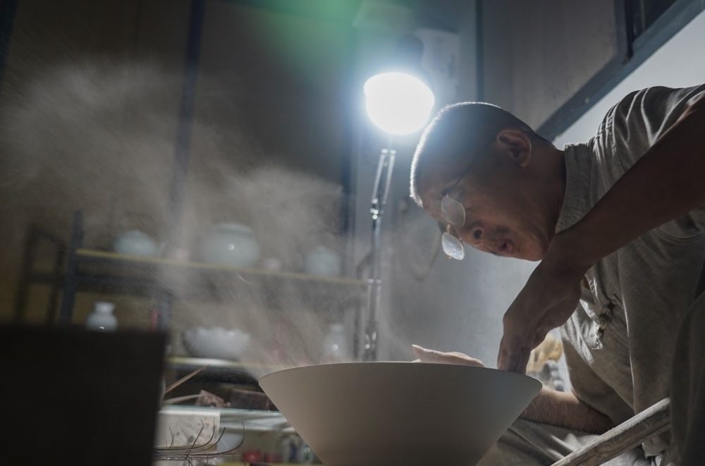 ↑ 在景德鎮(zhèn)，手工匠人吹去坯內(nèi)的泥土（2021年7月14日攝）。