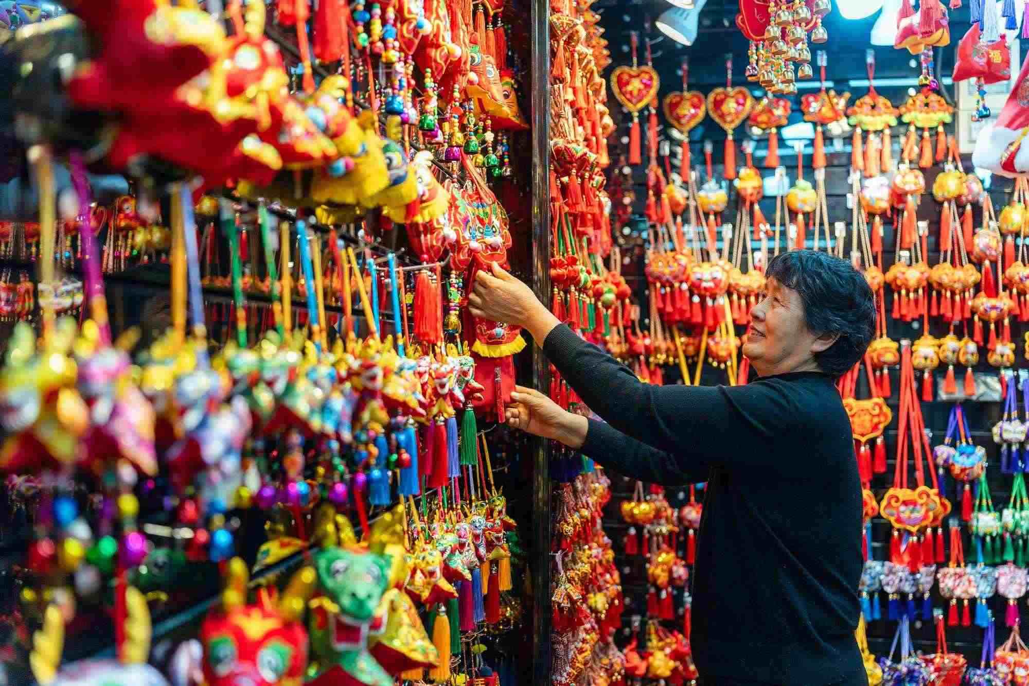 2023年12月11日，金華義烏國(guó)際商貿(mào)城，龍年喜慶用品掛滿攤位，顧客正在挑選中。