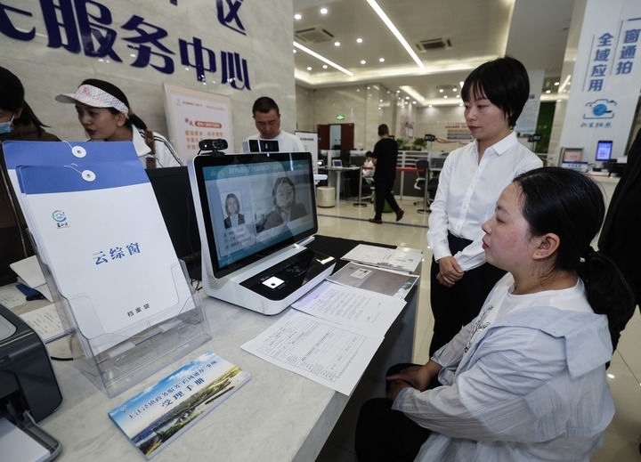 在浙江省嘉興市秀洲區(qū)王江涇鎮(zhèn)便民服務(wù)中心的“跨域通辦·云綜窗”窗口，辦理開業(yè)登記的個體工商戶（右一）通過該系統(tǒng)與江蘇省蘇州市吳江區(qū)盛澤鎮(zhèn)行政審批局工作人員視頻連線，進行身份讀取及材料線上審核（2024年5月9日攝）。新華社記者 徐昱 攝
