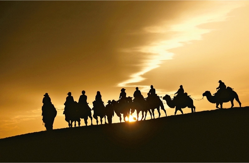 新時代以來，文化和旅游深度融合發(fā)展體制機(jī)制不斷健全，成功走出了一條獨(dú)具特色的中國旅游發(fā)展之路。圖為2024年9月1日清晨，游客在甘肅省敦煌市鳴沙山月牙泉景區(qū)乘騎駱駝，欣賞大漠風(fēng)光，體驗(yàn)絲路風(fēng)情。 新華社發(fā) 張曉亮/攝